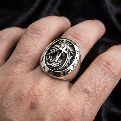 Close-up of a men's sterling silver gothic signet ring worn on a hand, featuring a central cross design with flame details surrounded by an engraved Roman numeral bezel against a dark background.
