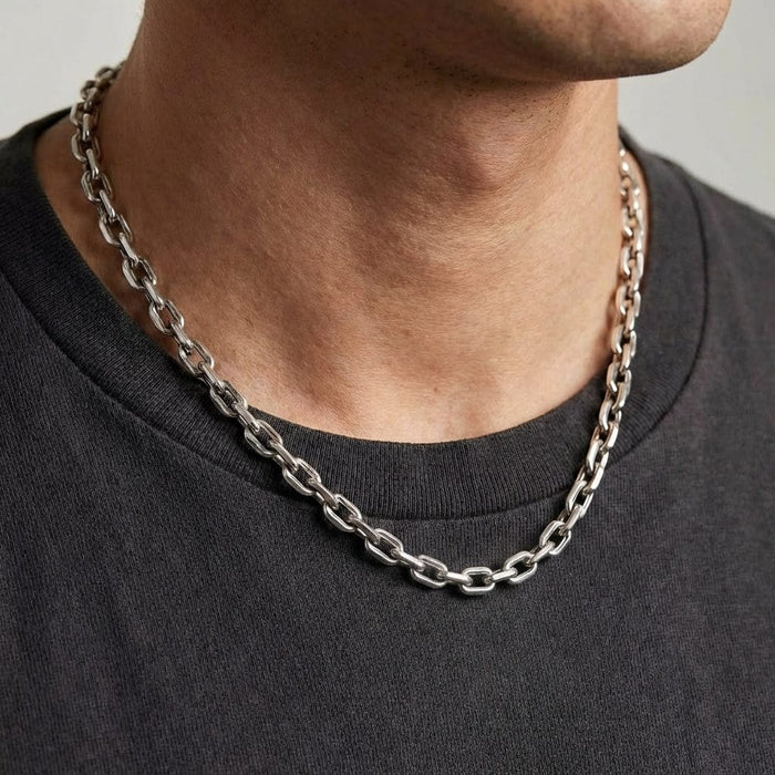 Man wearing a chunky silver cable chain link necklace with a dark gray crewneck shirt, showcasing the bold masculine jewelry style in a close-up lifestyle shot