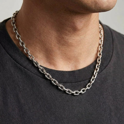 Man wearing a chunky silver cable chain link necklace with a dark gray crewneck shirt, showcasing the bold masculine jewelry style in a close-up lifestyle shot