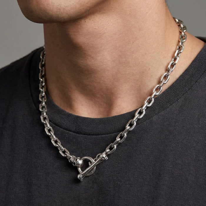 Silver skull bone toggle chain necklace worn by male model featuring chunky link chain with decorative skull clasp closure on dark gray t-shirt background