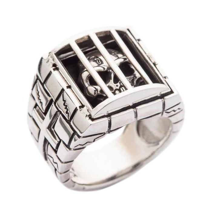 A solid sterling silver caged skull ring, featuring a detailed skull behind the bars of a prison cell with a stone wall band.