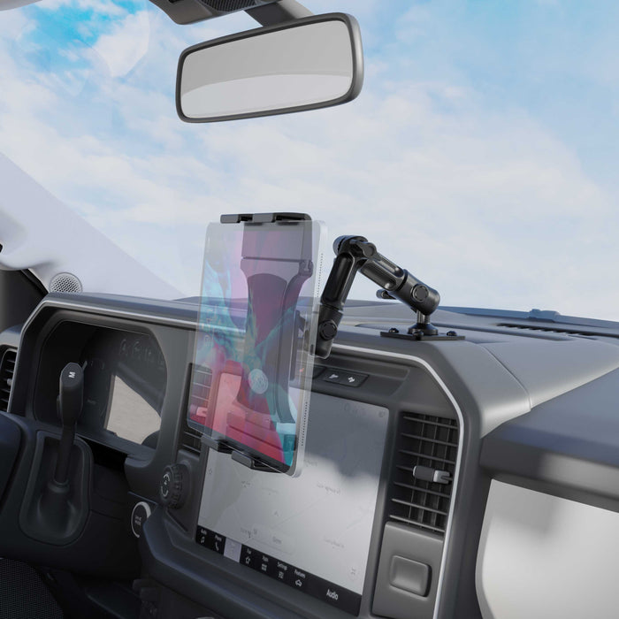 The Slim-Grip® Ultra Pro Tablet Holder with Multi-Angle Arm and Drill-Base Mount is securely attached to the vehicle’s dashboard above the infotainment screen, with a clear windshield and blue sky visible outside.
