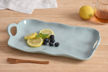 Light blue ceramic tray with lemon slices, blueberries, and a wooden fork on a wooden surface.