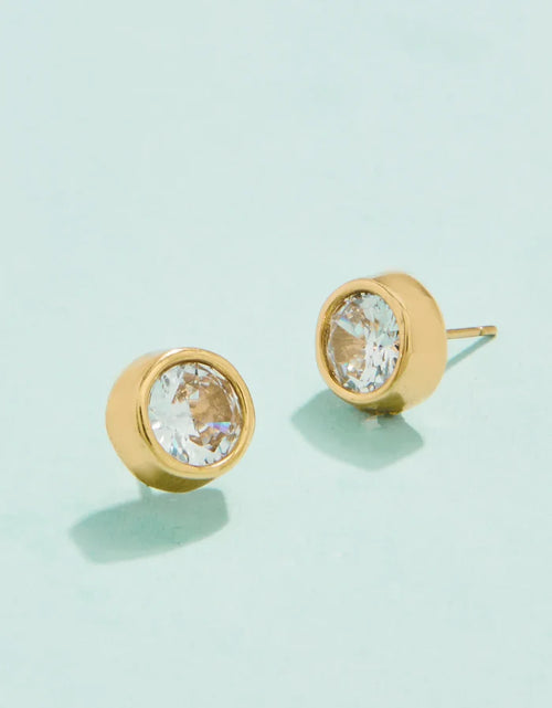 A pair of gold-colored stud earrings with cubic zirconia crystals on a light background.