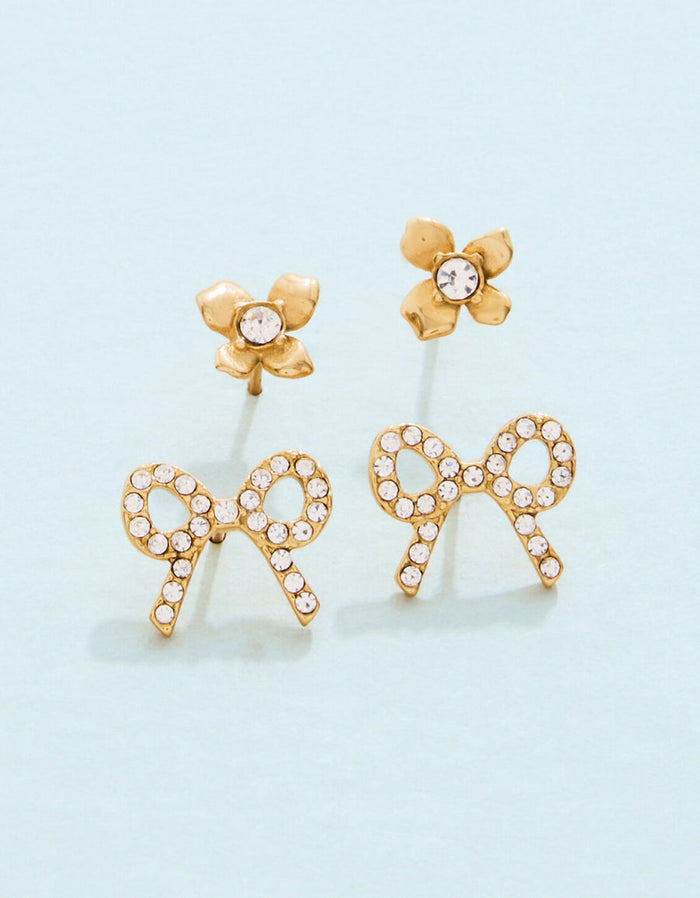Gold bow-shaped earrings with clear stones on a light blue background