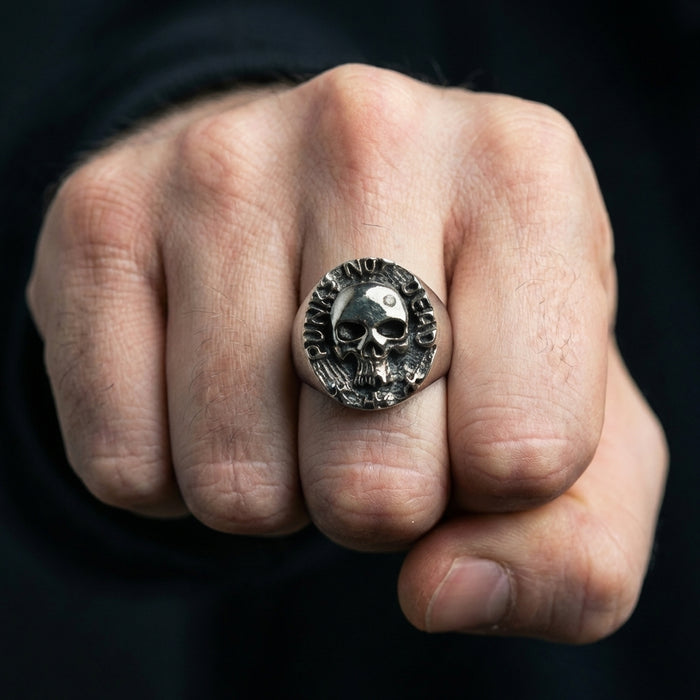 Close-up of a man's clenched fist wearing a silver Punk Not Dead skull ring against a dark background.