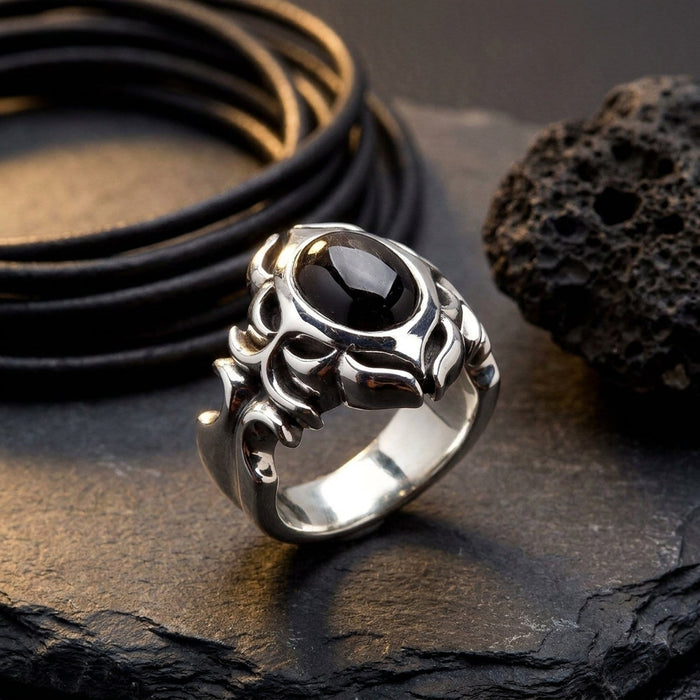 Editorial still-life of the black onyx tribal silver ring on dark slate beside a coiled leather cord under raking side light