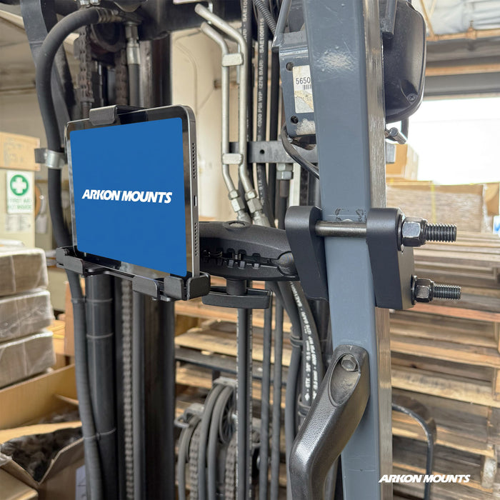 A tablet with a blue Arkon Mounts screen is securely held by the XMS™ Heavy Duty Forklift Mount with LockVise™ Metal Locking Tablet Holder, attached to a forklift and surrounded by pallets and warehouse equipment.