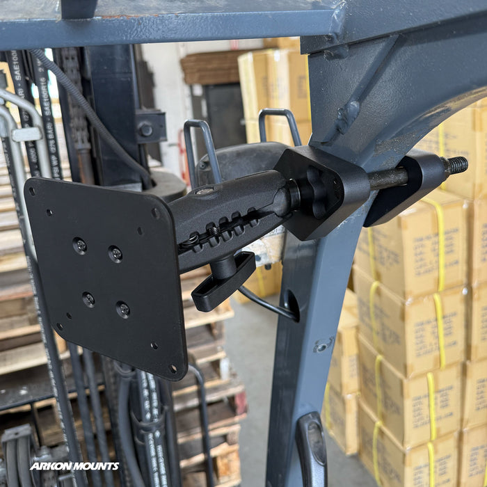The XMS™ Heavy Duty Forklift Mount with VESA Adapter Plate is attached to metal equipment in a warehouse setting featuring stacked cardboard boxes and forklift parts.